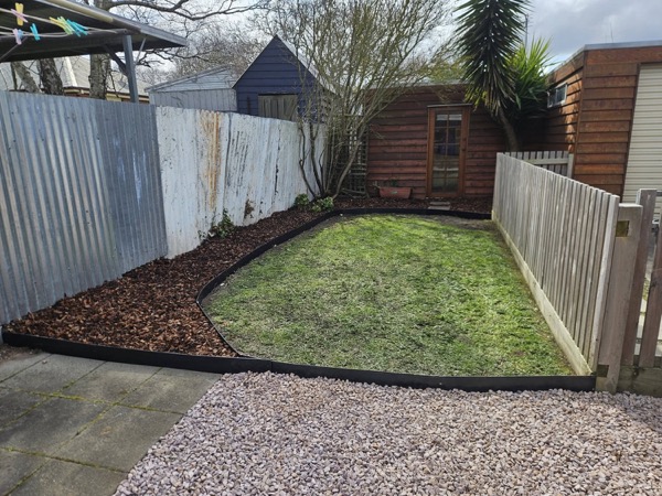 A back lawn with a curved mulched garden bed and a pebbled strip along the fence