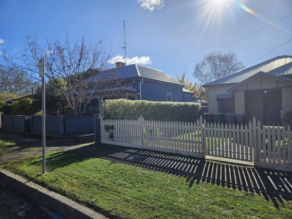 A trimmed hedge and white picket fence in front of a weatherboard cottage