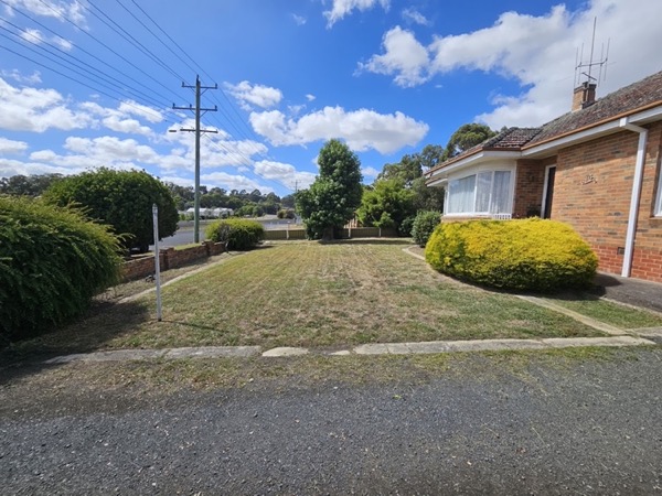 A mown front lawn and driveway in front of a brick house
