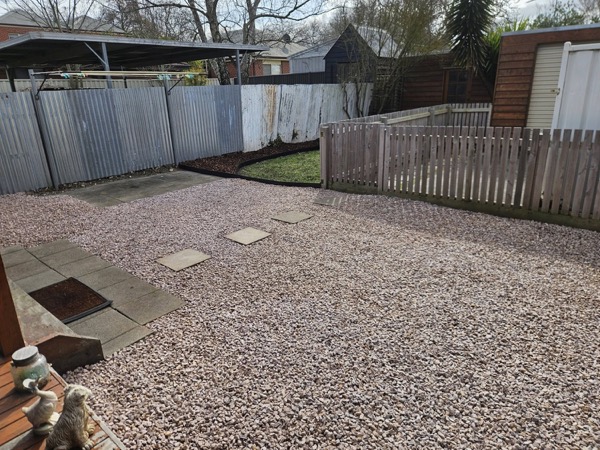A back yard finished in pebble with concrete pavers set into it