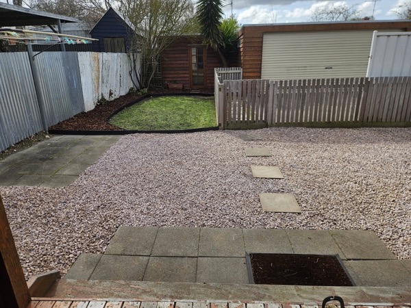 A pebbled back yard with pavers, edged against a timber fence