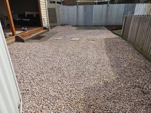 A pebbled yard with pavers laid between a corrugated fence and the house