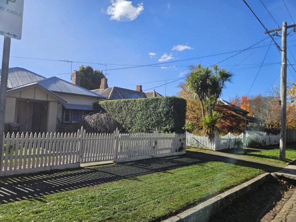 A mown nature strip and trimmed hedge along a white picket fence