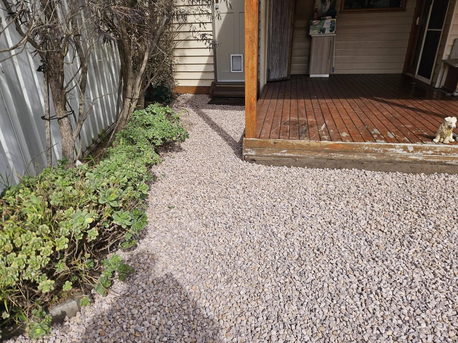 A pebbled yard with stepping stones running to a timber deck